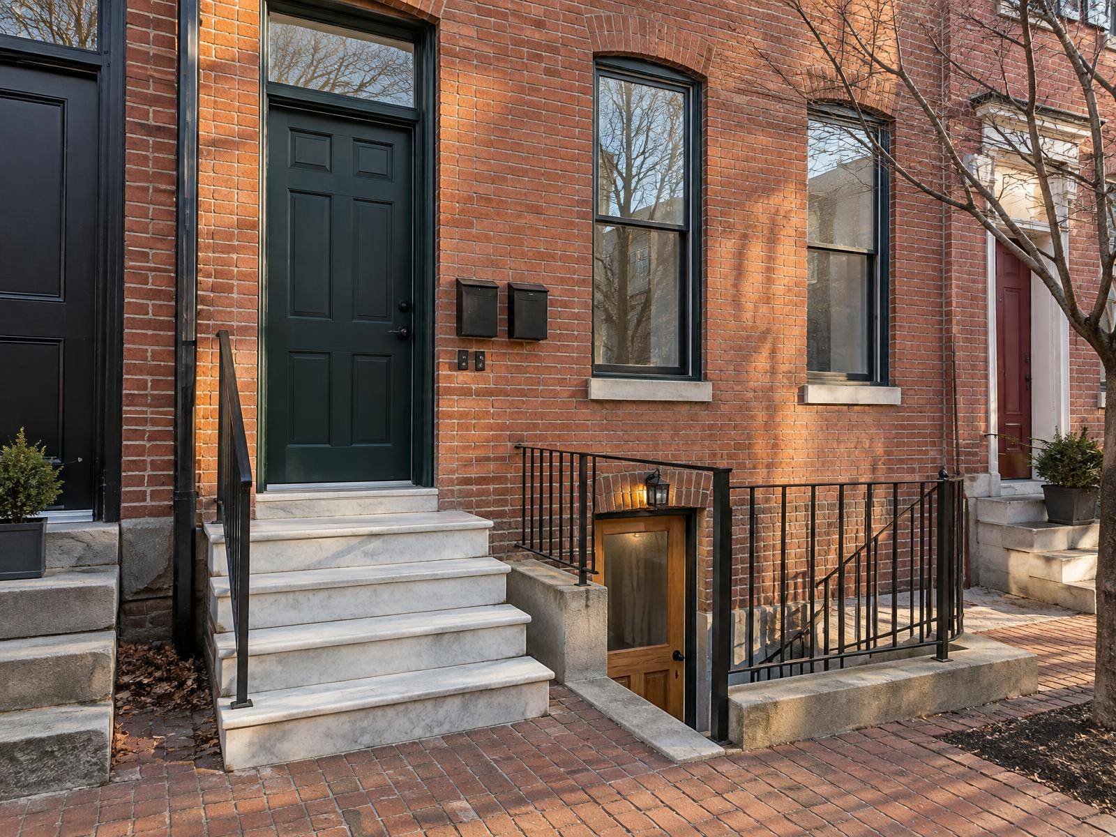 Illustration of a Baltimore brick rowhouse being converted to two units, with a new basement apartment door at the bottom of areaway steps beside the white marble front stoop and a second mailbox by the main entrance above.