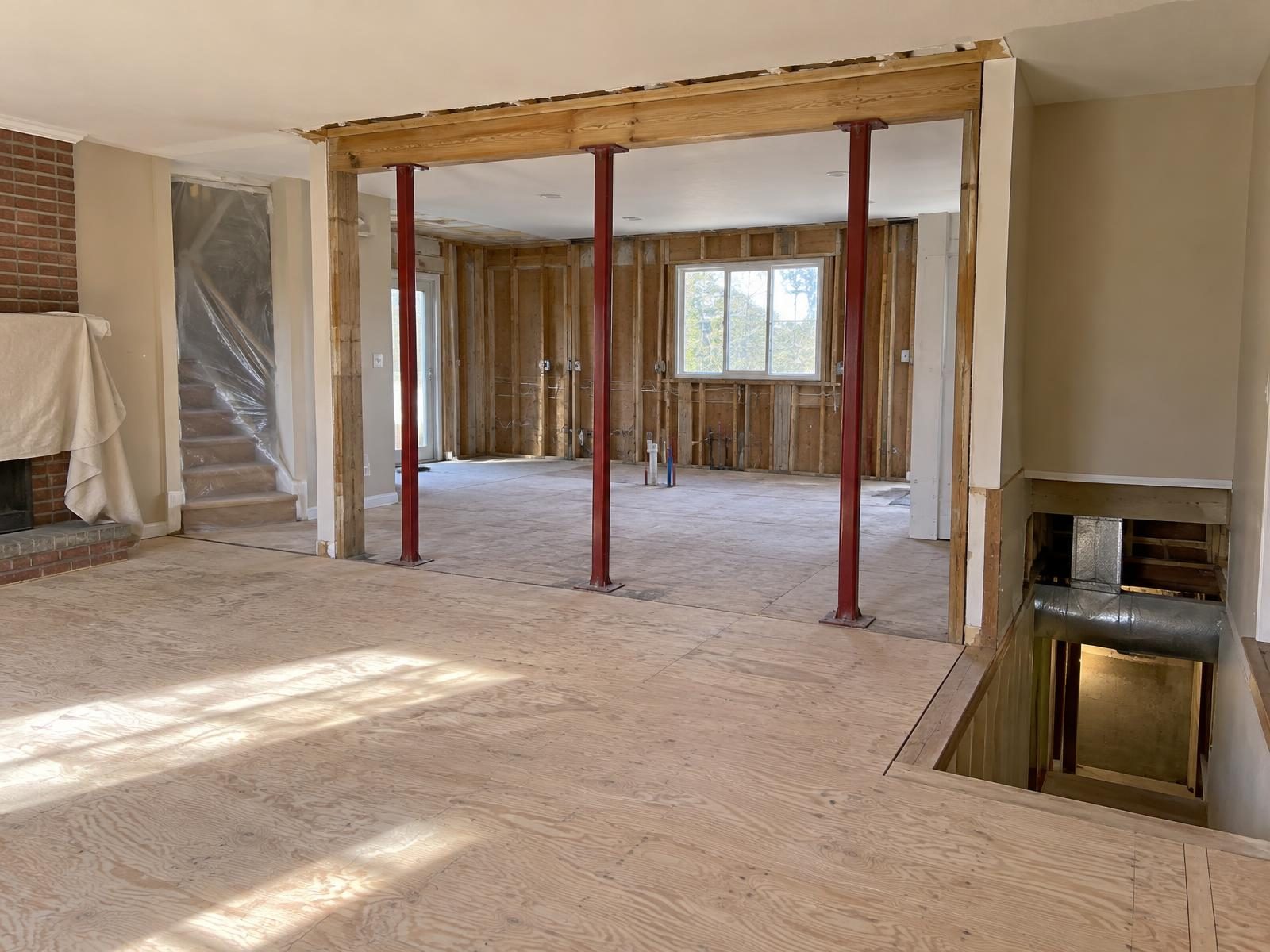 Illustration of a 1980s Fairfax County colonial in the middle of a whole-house renovation, with the wall between kitchen and family room opened on temporary steel supports, the kitchen stripped to the studs, new ductwork visible down the open basement stairway and plastic sheeting hung over the stairs to the second floor.