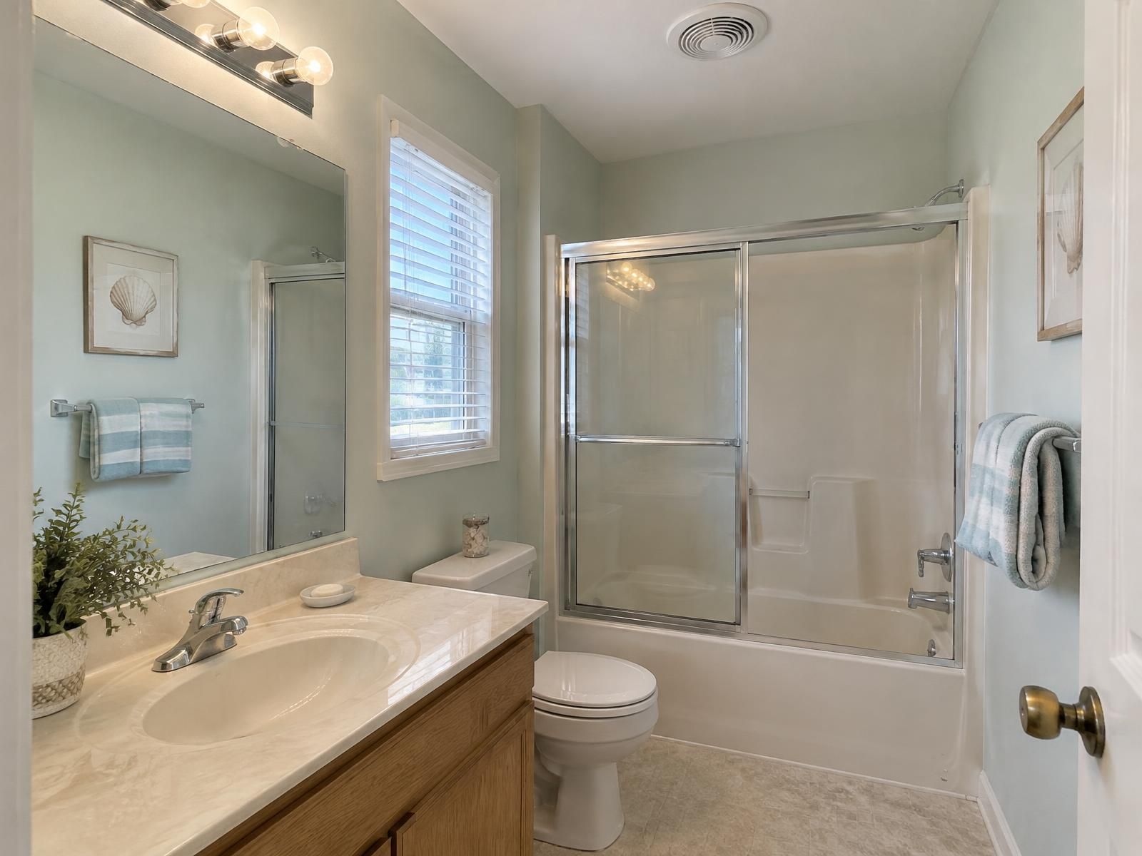Illustration of an upstairs hall bathroom in a 1980s Virginia Beach two-story: a fiberglass tub-shower, a cultured-marble vanity top on an oak cabinet, and a ceiling exhaust fan ducted outdoors to clear the humid coastal air.